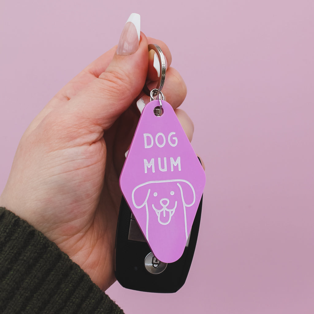 Hand holding a pink Motel Style keychain with 'DOG MUM' text and dog illustration against a pink background