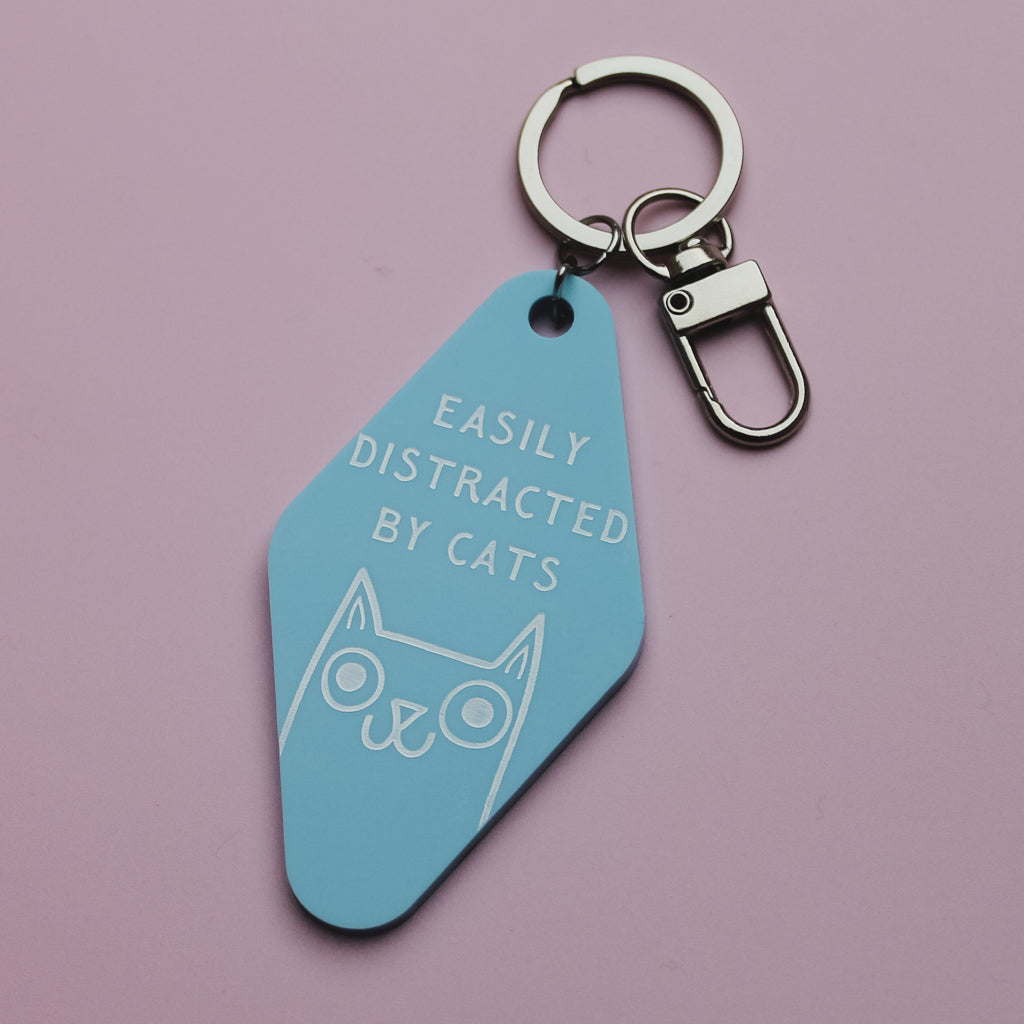 Blue motel style keyring with 'Easily Distracted by Cats' text and cat illustration on a pink background