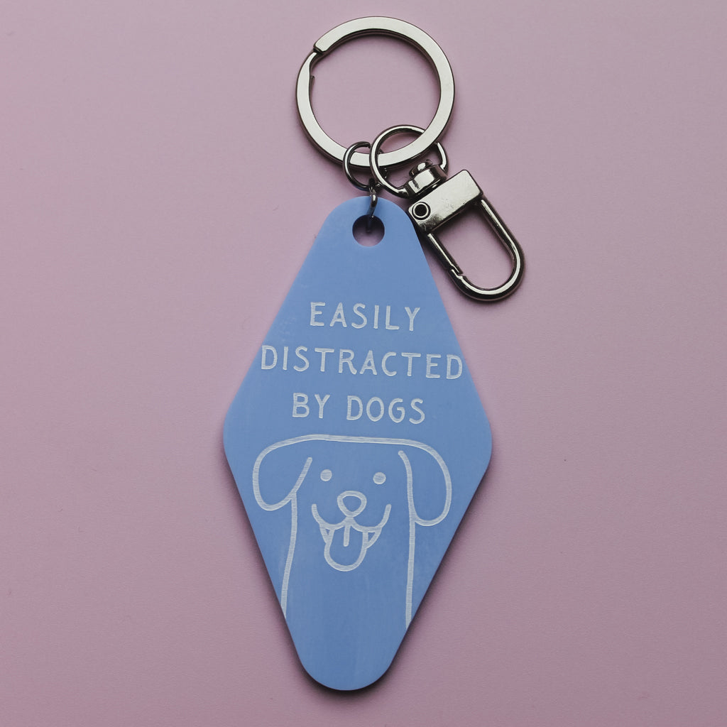 Blue motel style keychain with 'Easily Distracted by Dogs' text on a pink background