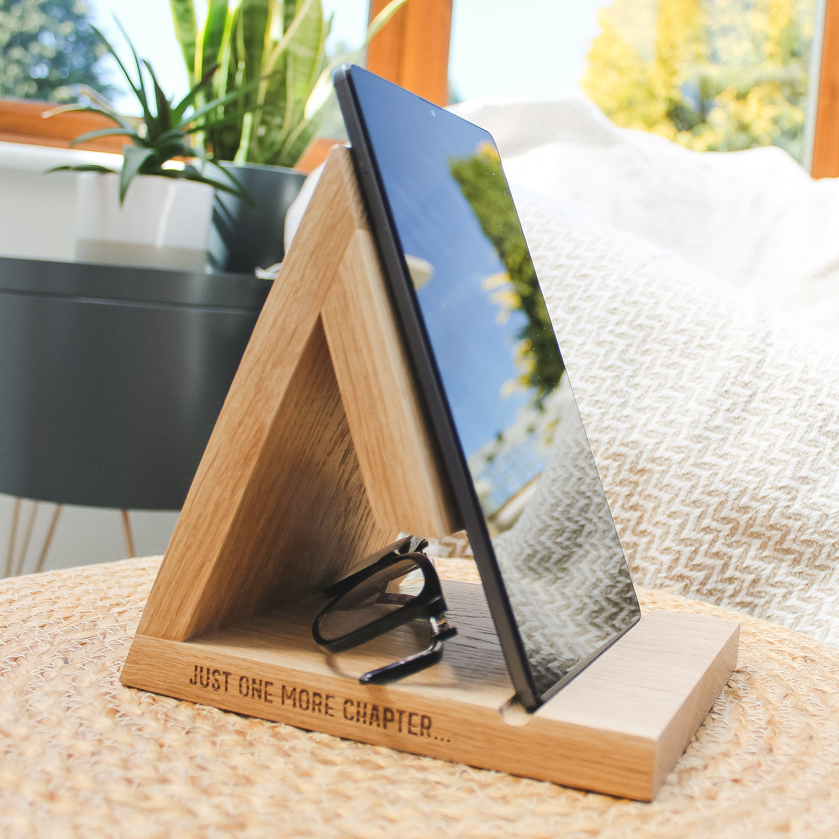 A triangular oak, wooden e-reader stand with the engraved text 'JUST ONE MORE CHAPTER.