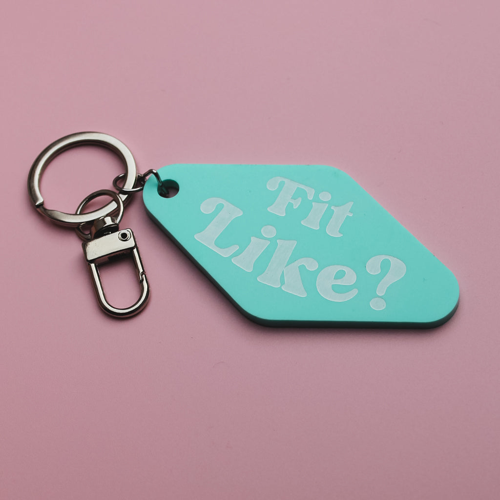 Turquoise motel style keychain tag with 'Fit Like?' text on a pink background