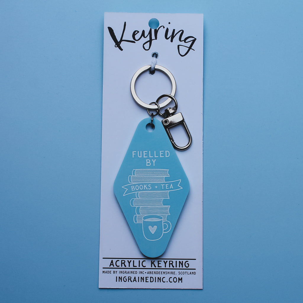Blue acrylic motel style keyring with text saying fuelled by books and tea on a white backing card against a blue background