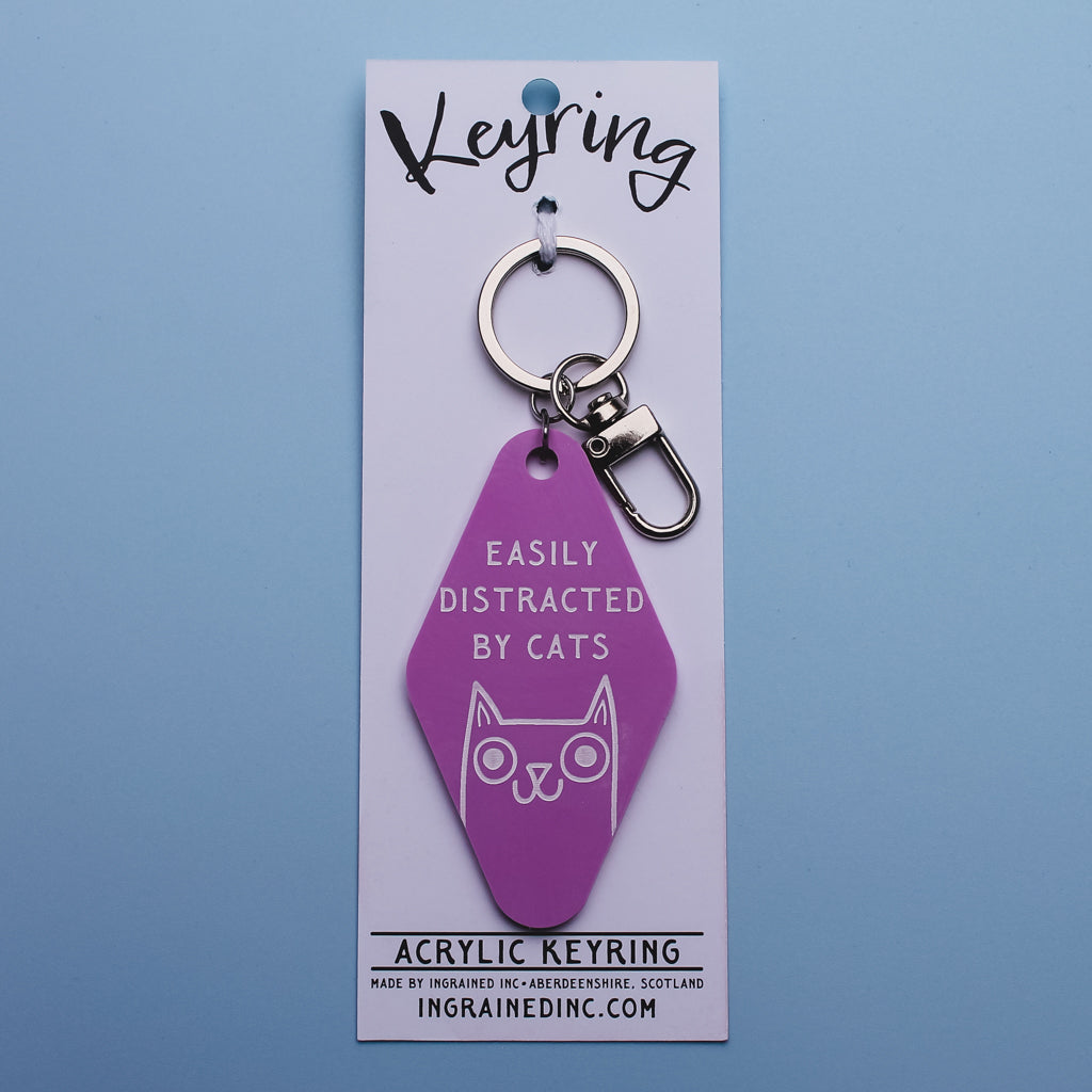 Pink keyring with 'Easily Distracted by Cats' text and cat design attached to white backed packaging on a blue background