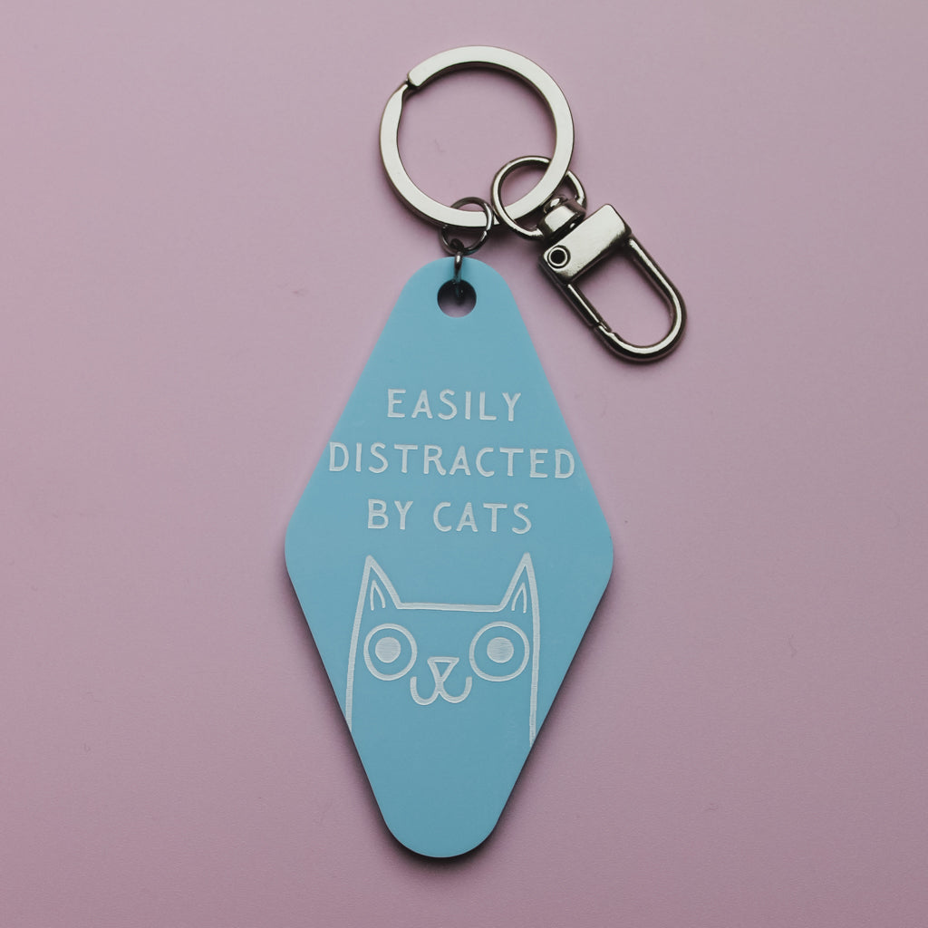 Blue motel style keyring with 'Easily Distracted by Cats' text and cat illustration on a pink background
