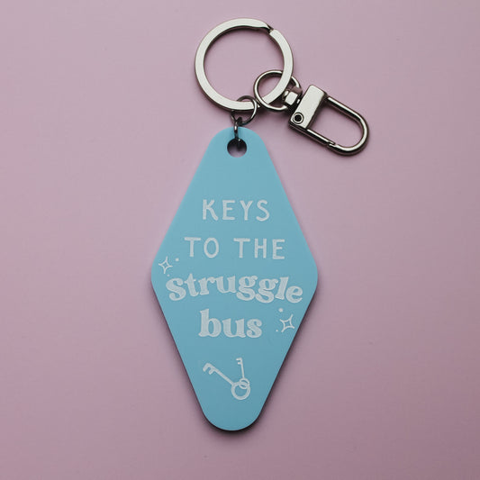 Blue motel style keychain with 'Keys to the Struggle Bus' text on a pink background