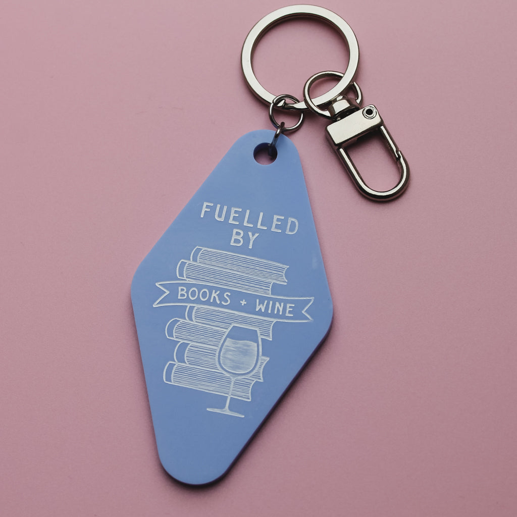Blue motel style keyring with 'Fuelled by Books + Wine' text on a pink background