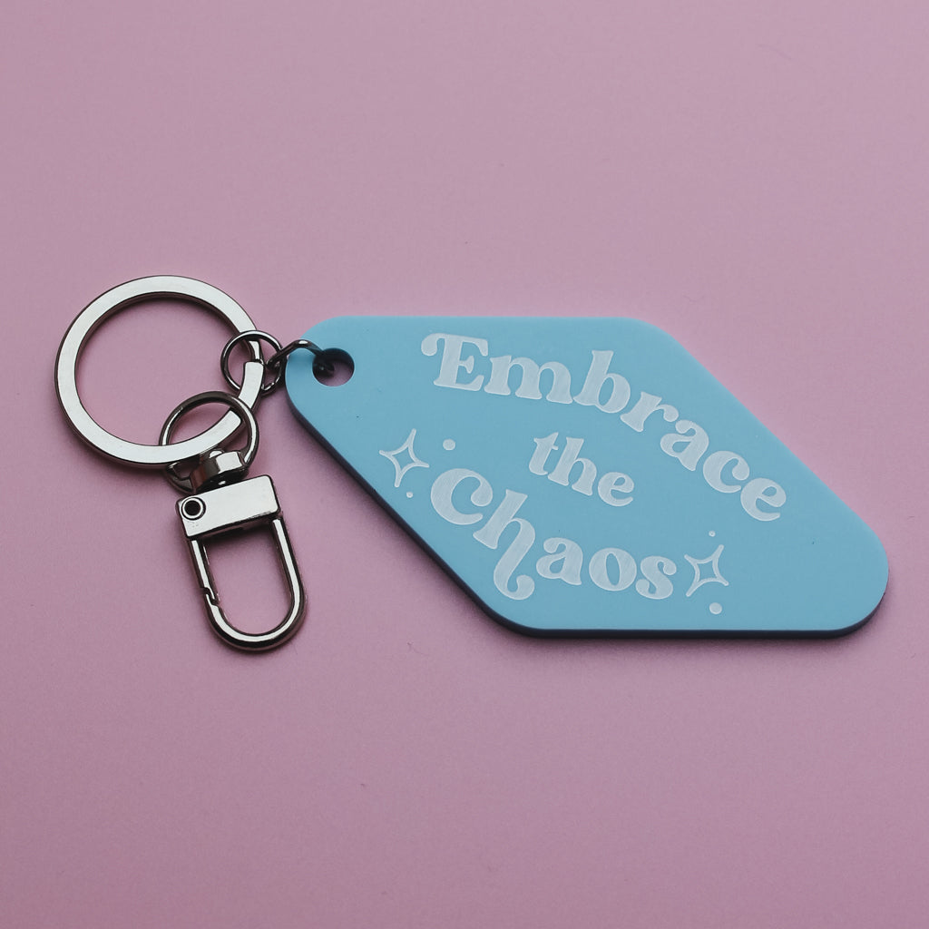 Motel style keyring with a blue tag that says 'Embrace the chaos' on a pink background