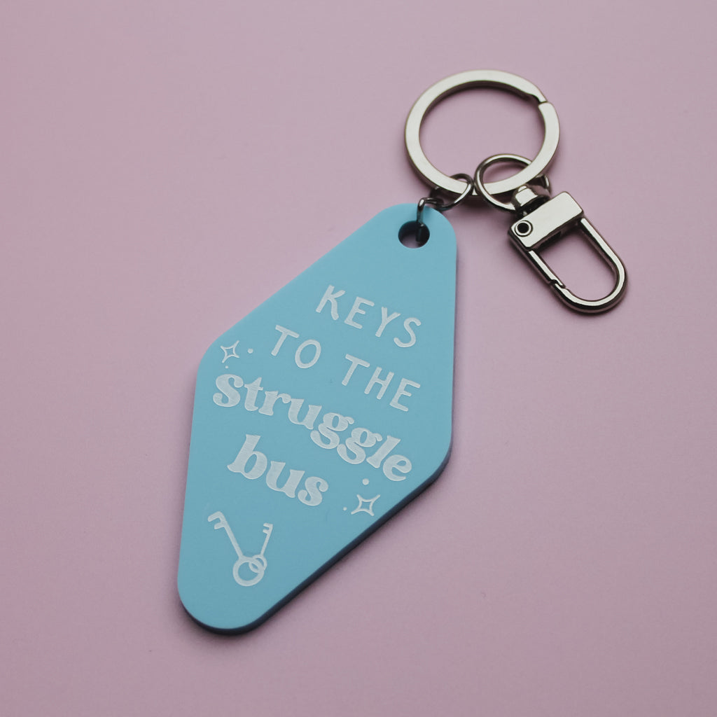 Blue motel style keychain with 'Keys to the Struggle Bus' text on a pink background