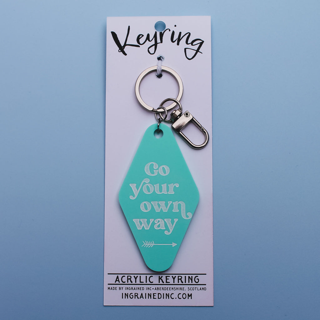 Teal acrylic motel style keyring with 'Go your own way' text on a white backing card against a light blue background