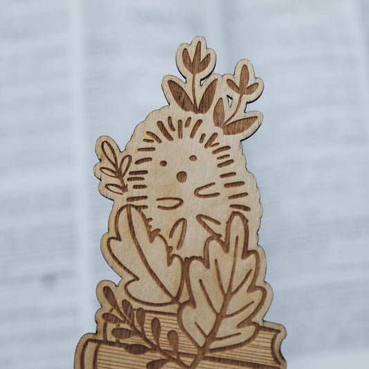 wooden hedgehog and leaf designed bookmark sitting on an open book in the background 
