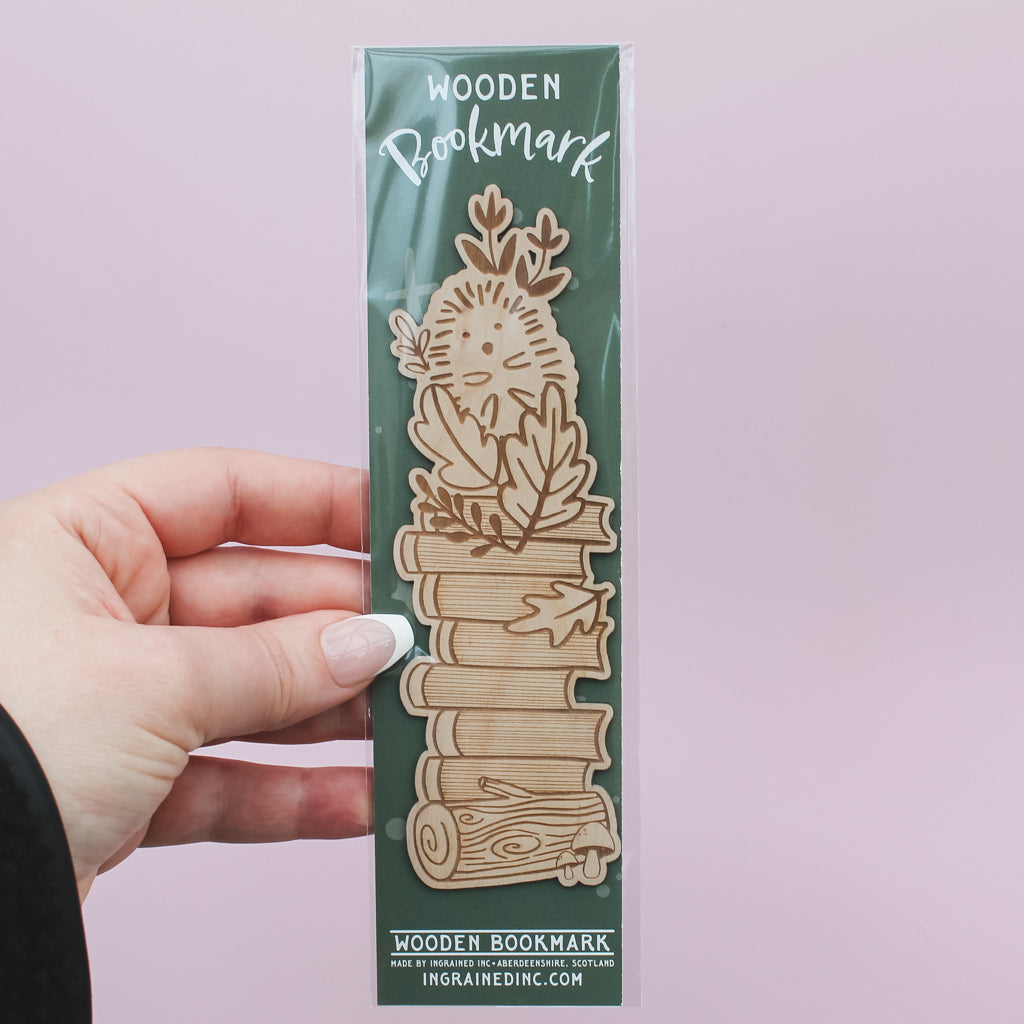Wooden hedgehog bookmark in packaging held by a hand on a light pink background