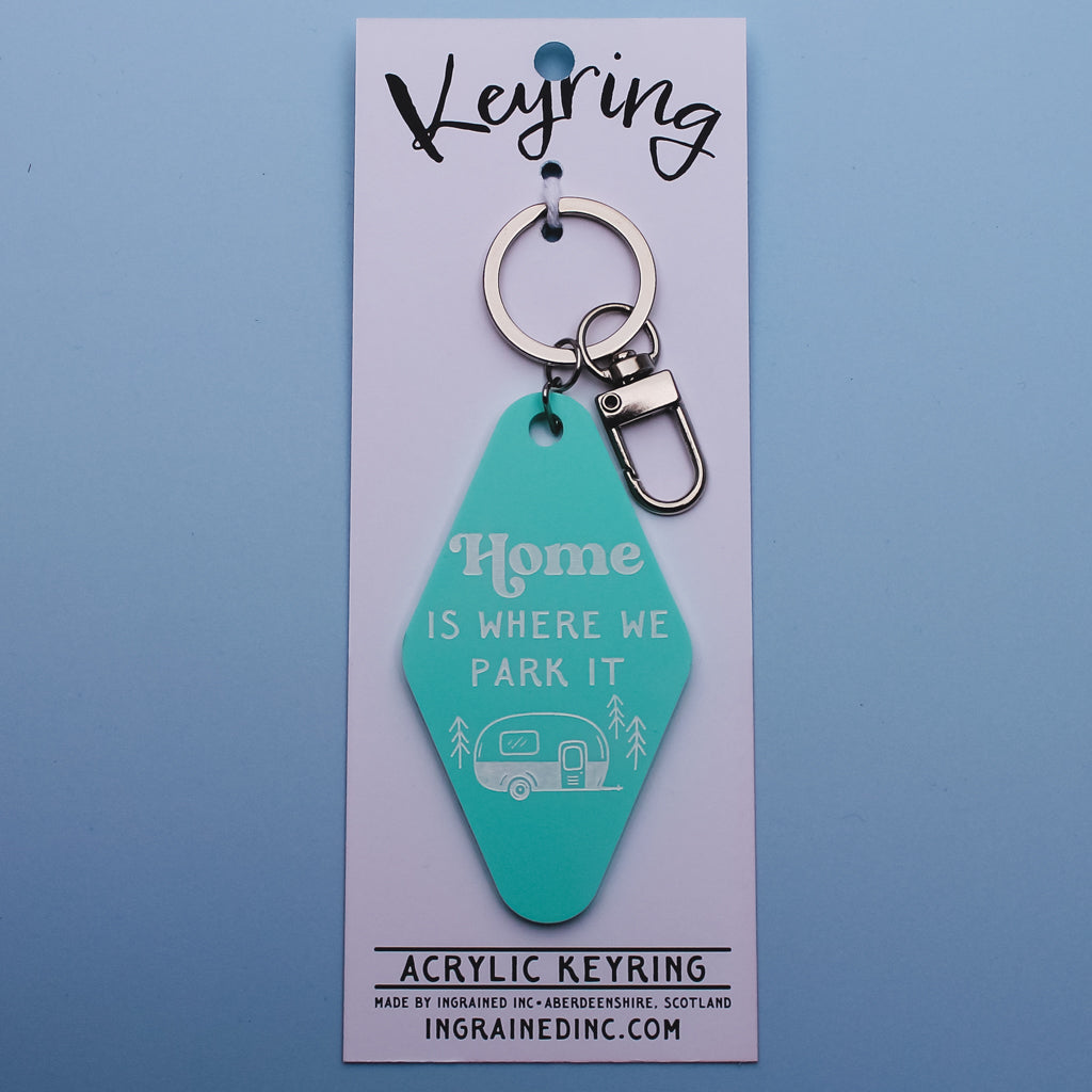 Turquoise motel style keyring with 'Home is where we park it' text on a backing card against a blue background