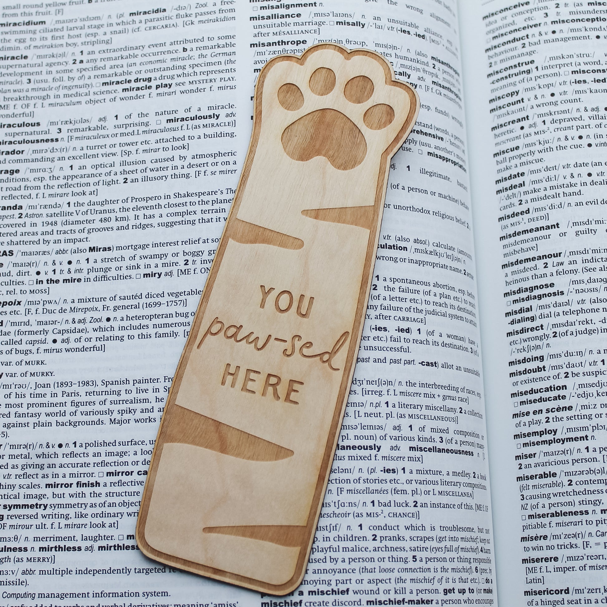 Wooden cat paw shaped bookmark with paw print design, sitting on an open book. Engrvaved with the text 'you paw-sed here' 