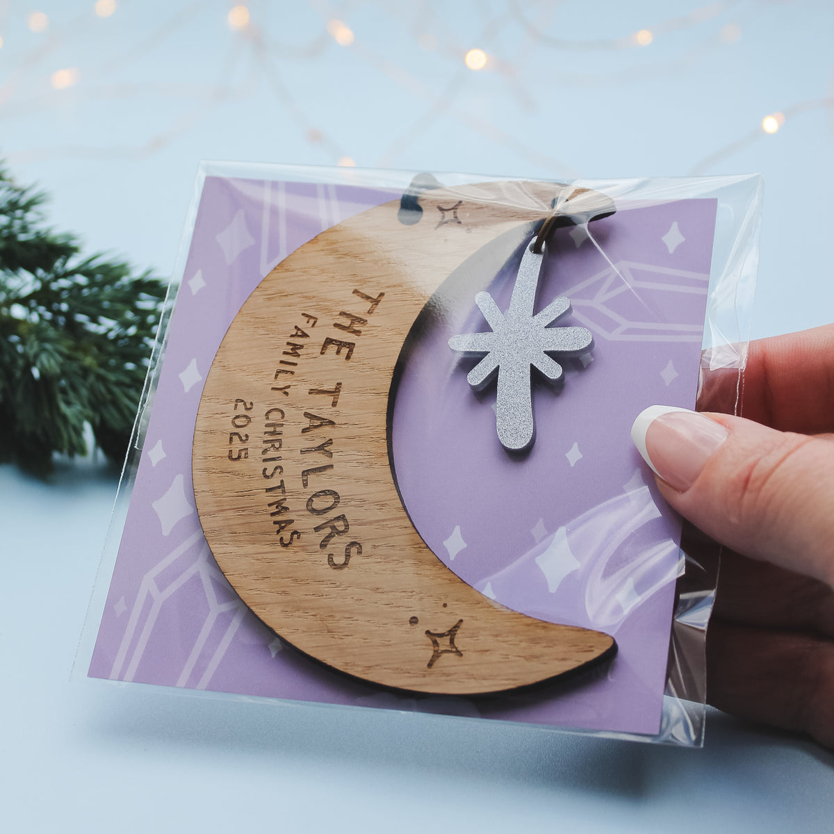 Wooden crescent moon ornament with personalised newlywed couple surname  engraved. Held in its purple packaging

