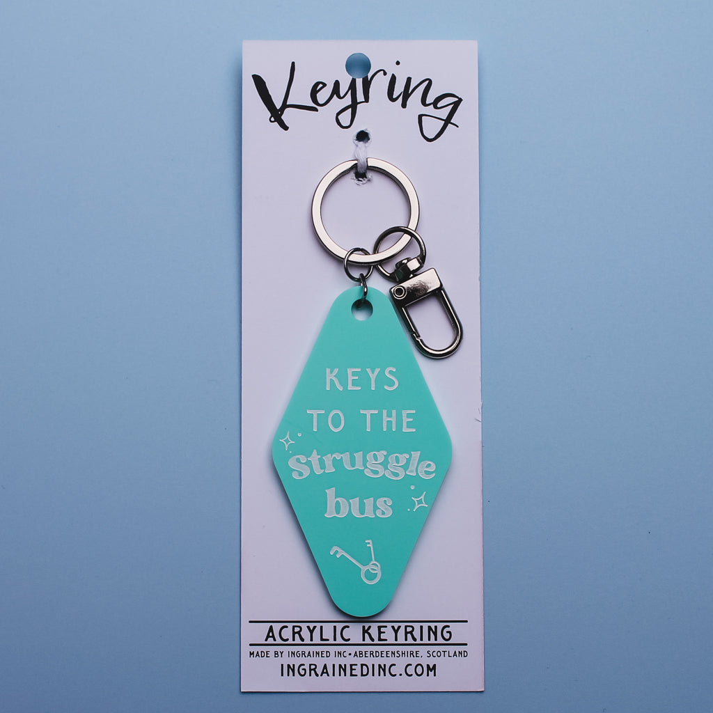 Turquoise motel keyring with 'Keys to the Struggle Bus' text on packaging card against a blue background