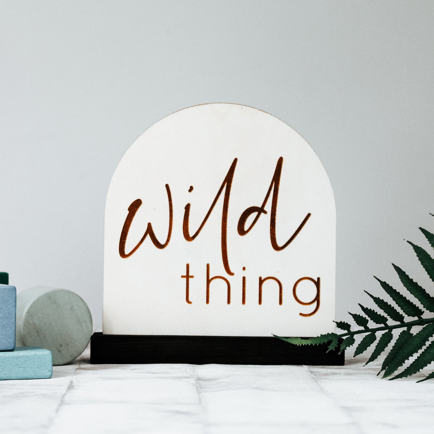natural wooden nursery sign engraved with the phrase wild thing and sat onto of a wooden sign holder