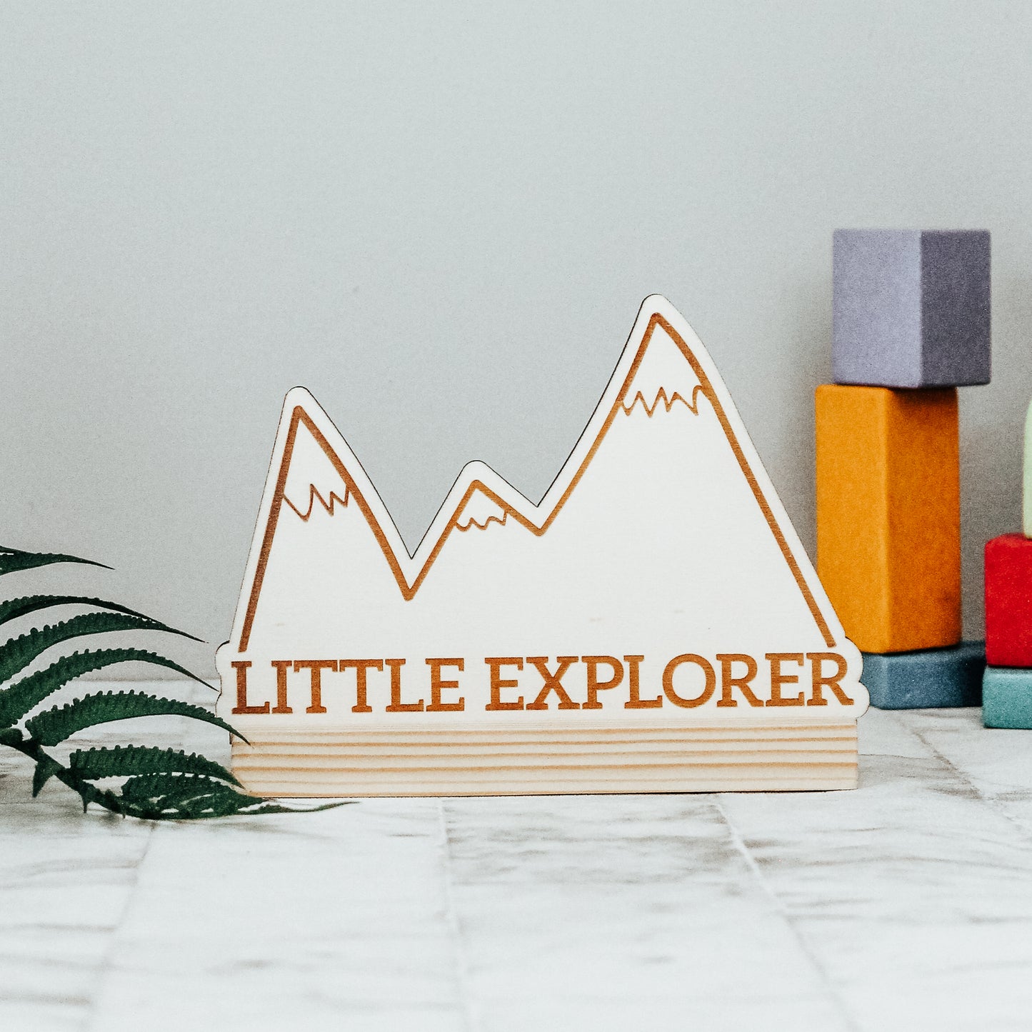 little explorer wooden standing nursery sign with mountain scandi design, sitting on the plain natural wooden base
