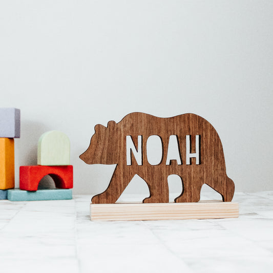 wooden bear silhouette with a name cut out of the body of the bear. the dark wooden colour bear sits on a natural light wooden coloured base and is a perfect gift for a nature inspired nursery