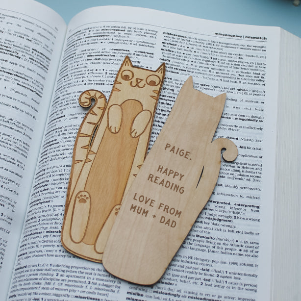 Wooden cat-shaped bookmarks on an open book with personalised engraved text.