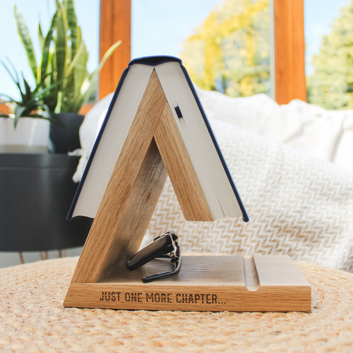 A warm oak wooden A-frame book stand engraved with 'JUST ONE MORE CHAPTER'.