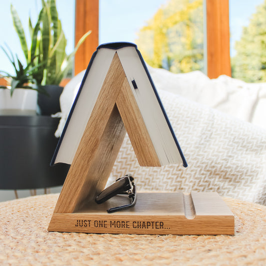 A warm oak wooden A-frame book stand engraved with 'JUST ONE MORE CHAPTER'.