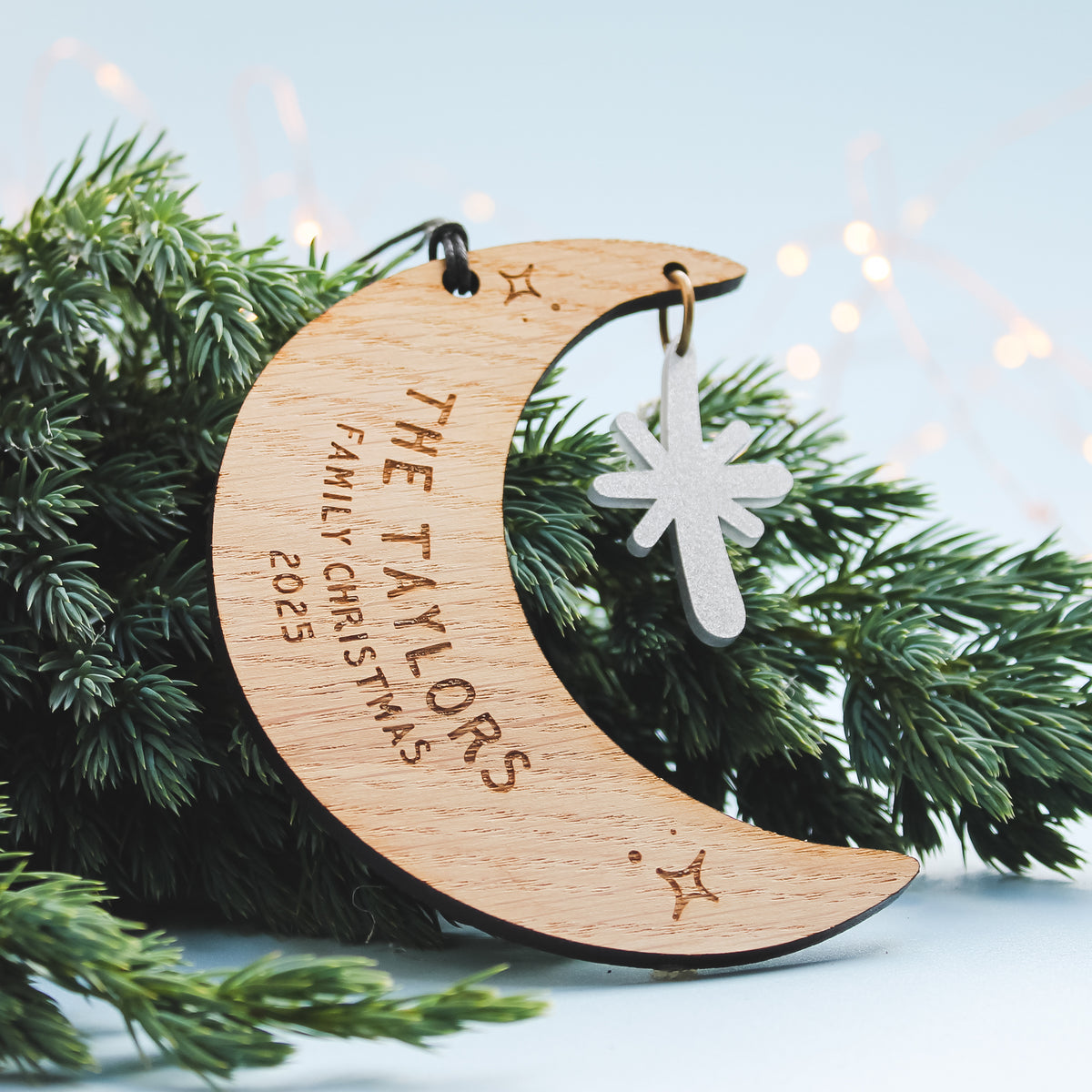 Wooden crescent moon ornament with personalised newlywed couple surname  engraved. Sitting on a Christmas tree.