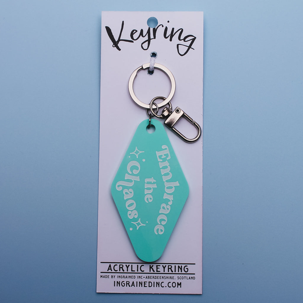 Teal motel style keyring with 'Embrace the Chaos' text on a white backing card against a blue background