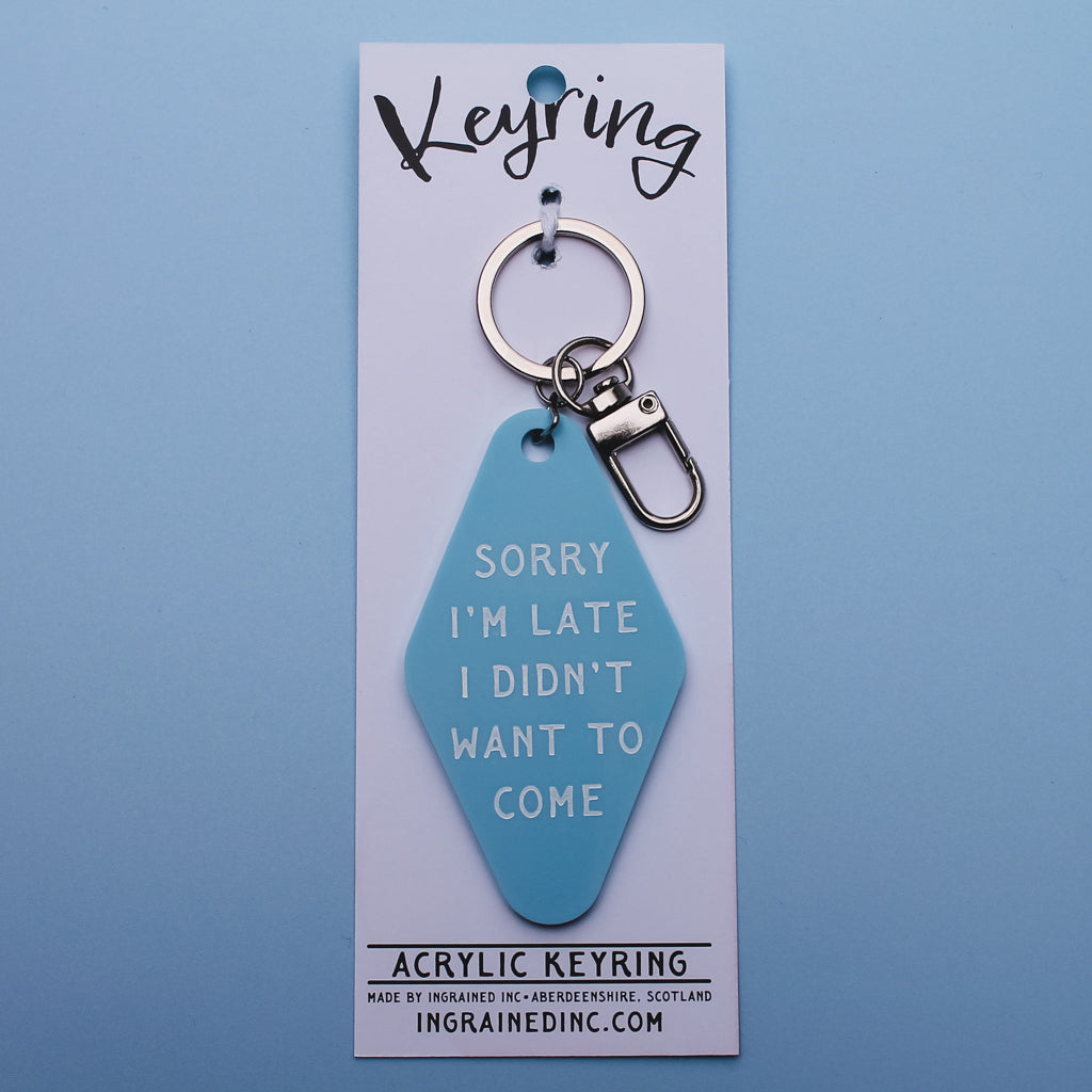Blue Motel style keyring tag with white text saying 'sorry i'm late I didn't want to come' in its packaging on a blue background