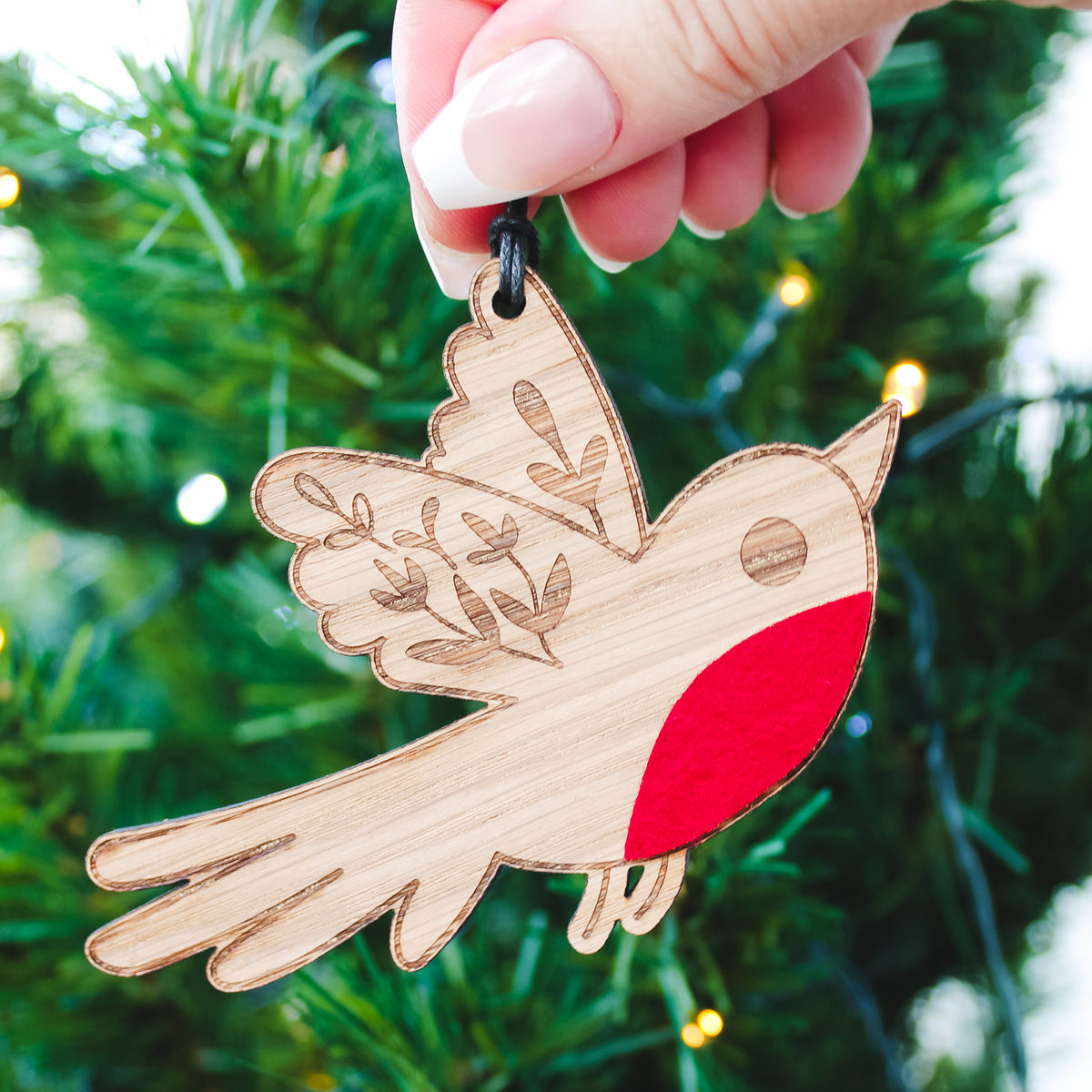 Wooden robin ornament with a red belly held in front of a Christmas tree.