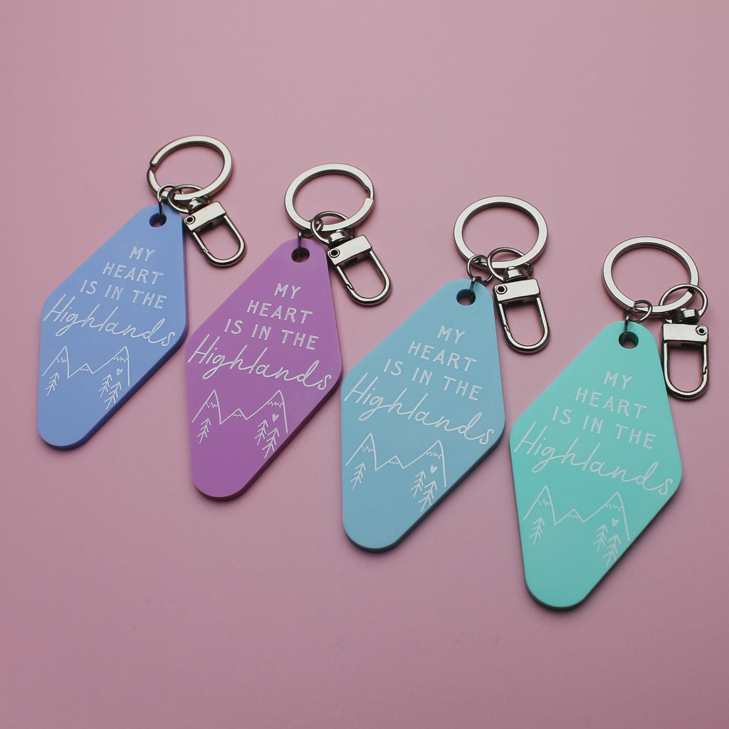 Four motel style keychains with 'My heart is in the Highlands' text on a pink background