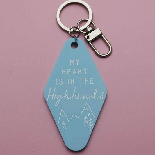 Blue motel style keychain with 'My heart is in the Highlands' text on a pink background