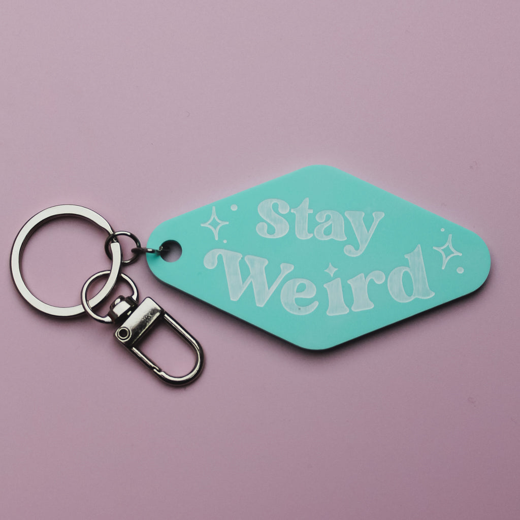 Turquoise motel style keychain with 'Stay Weird' text on a pink background