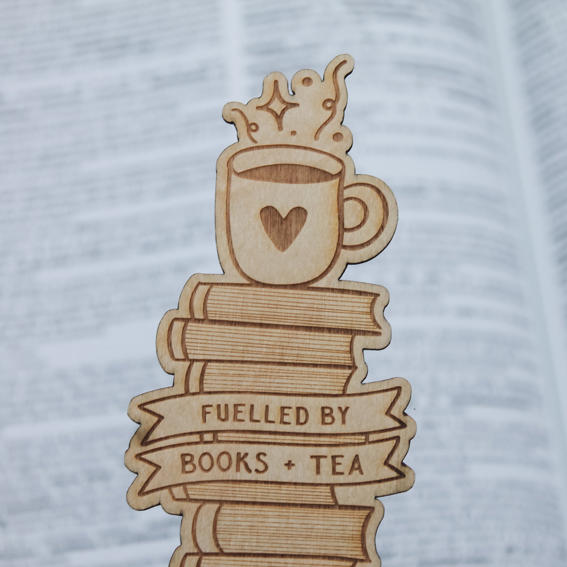 Wooden bookmark with a design of a mug, books, and 'Fuelled by Books + Tea' text on a textured background.