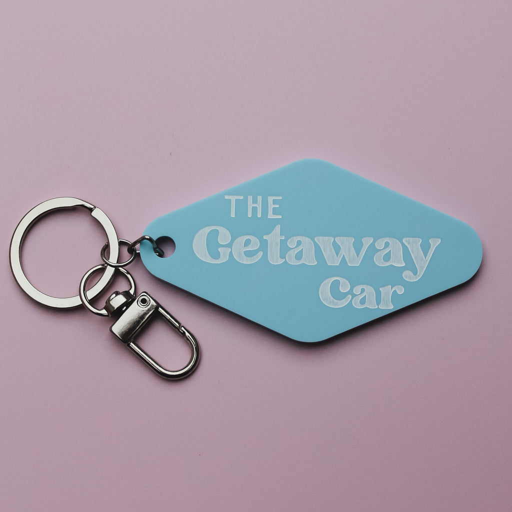 Blue motel style keychain tag with 'The Getaway Car' text on a pink background