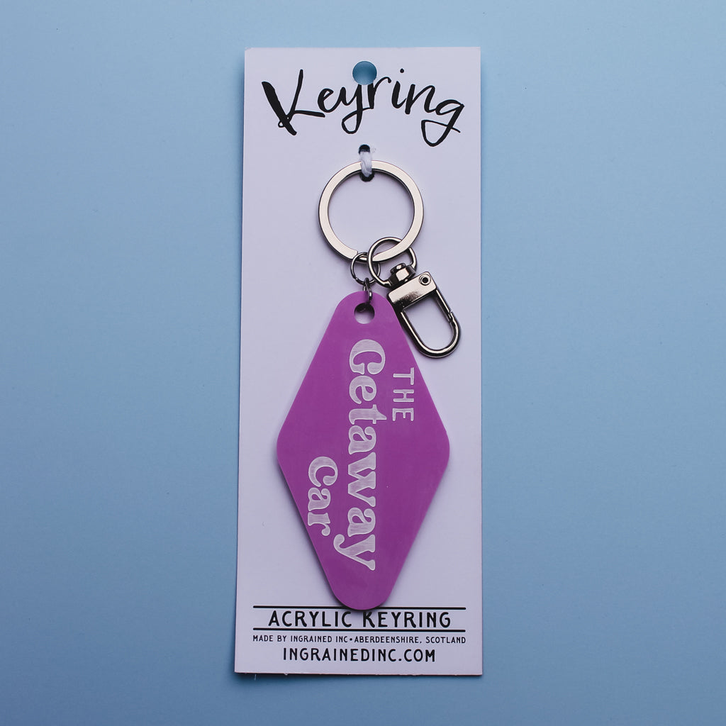 Pink motel style keyring with 'The Getaway Car' text on a white backing card against a blue background