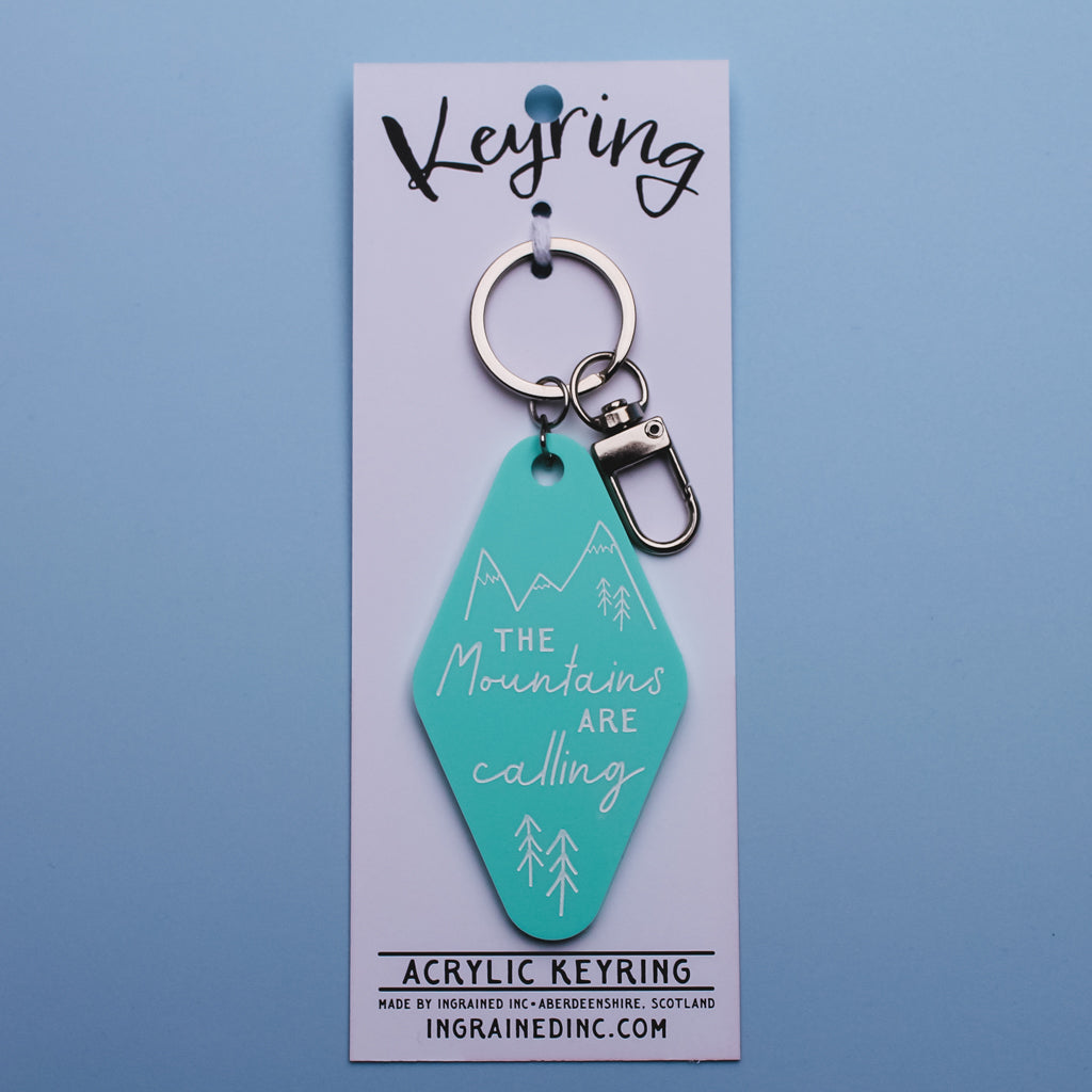 Teal motel style keyring with mountain design and text on a white backing card against a blue background