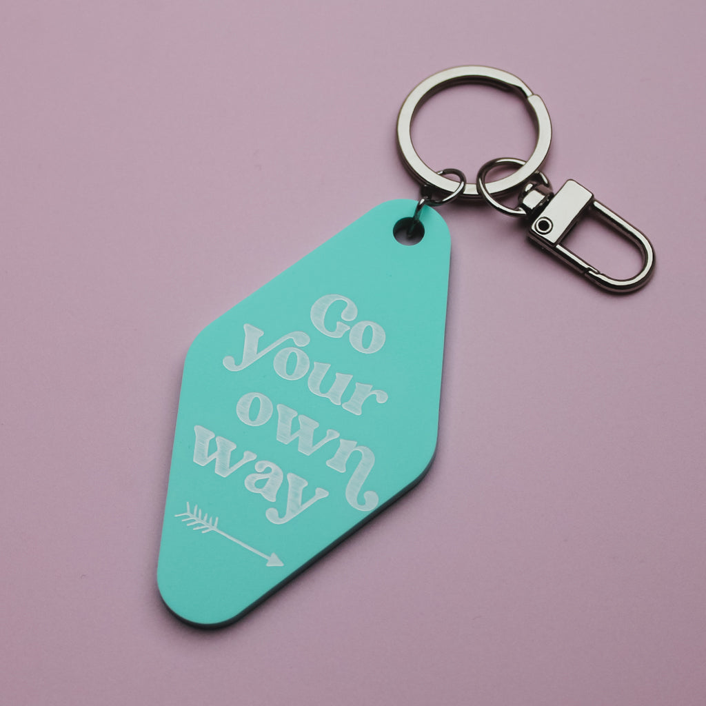 Turquoise motel style keychain with 'Go your own way' text on a pink background