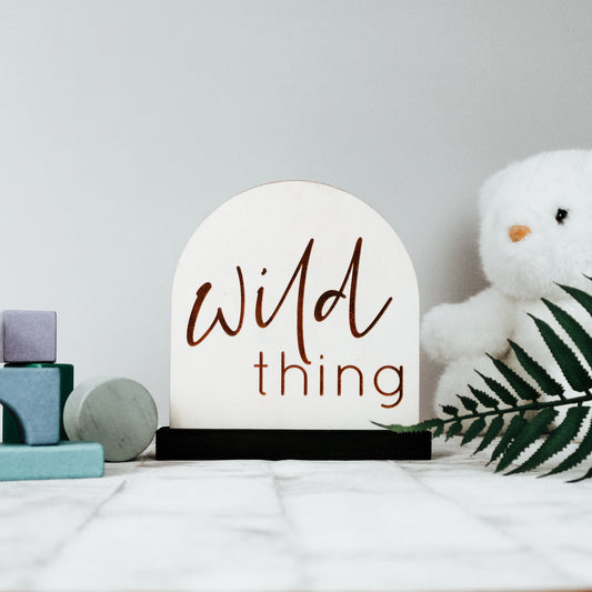 modern wooden nursery sign for a neutral colour nursery, the sign is engraved with the words wild thing and comes sitting on a wooden plinth 