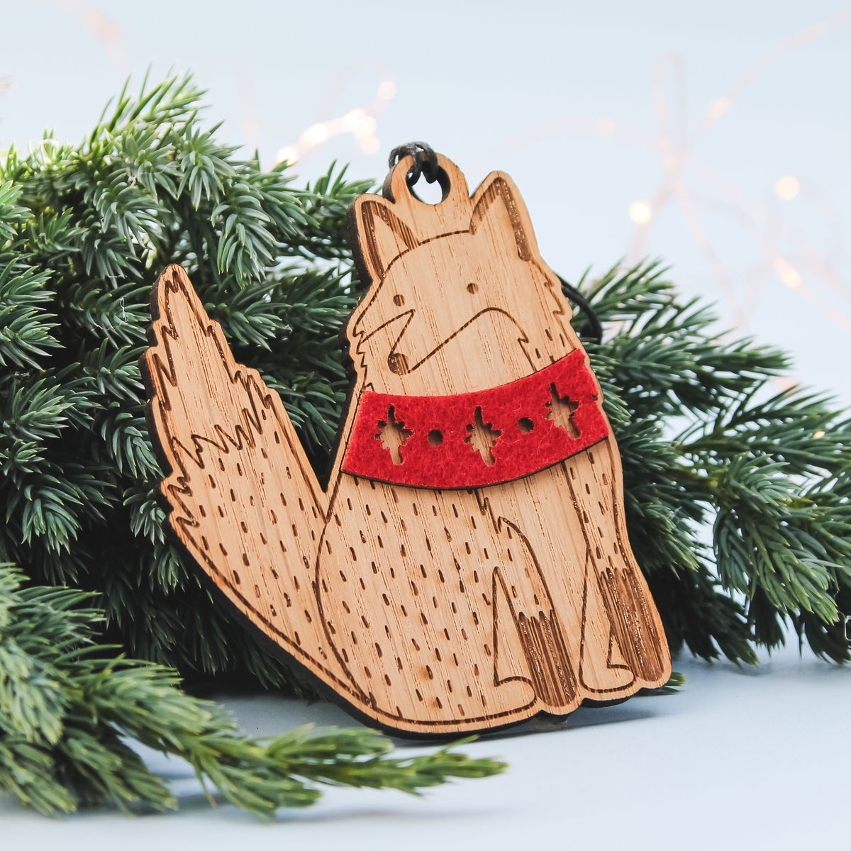 wooden fox in winter scarf Christmas decoration sitting on a Christmas tree  branch with twinkling lights behind 