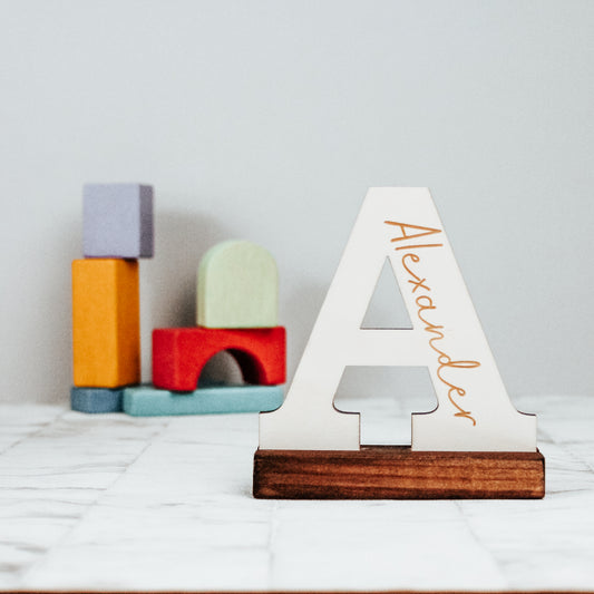 wooden capital letter standing on a base engraved with a name inside the letter an ideal new baby gift for a nursery shelf or bookcase 