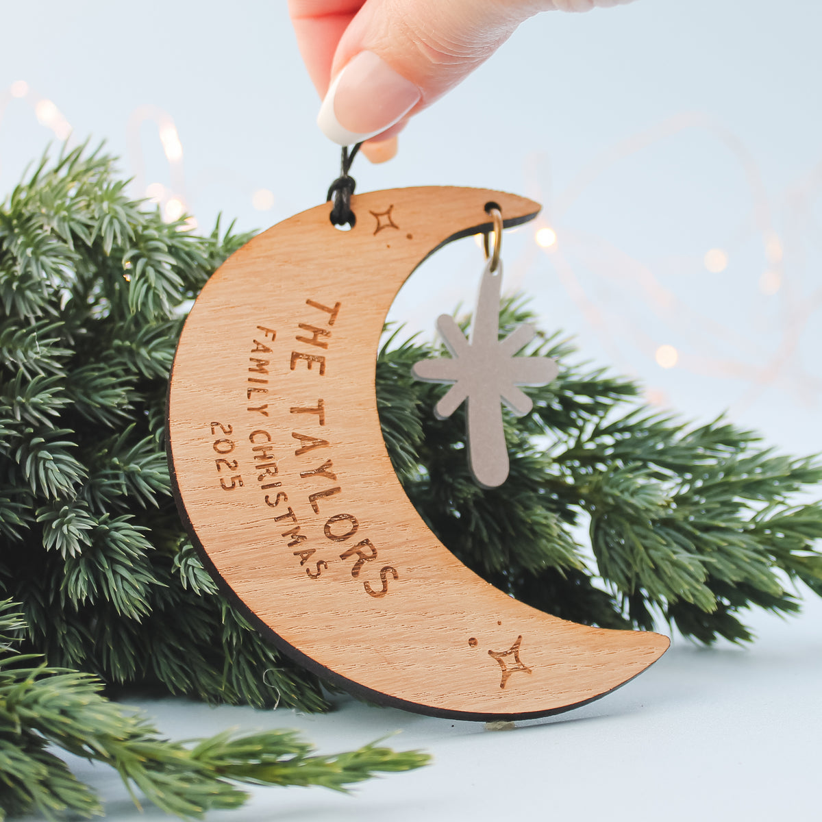 Wooden crescent moon ornament with personalised newlywed couple surname  engraved. Sitting on a Christmas tree.
