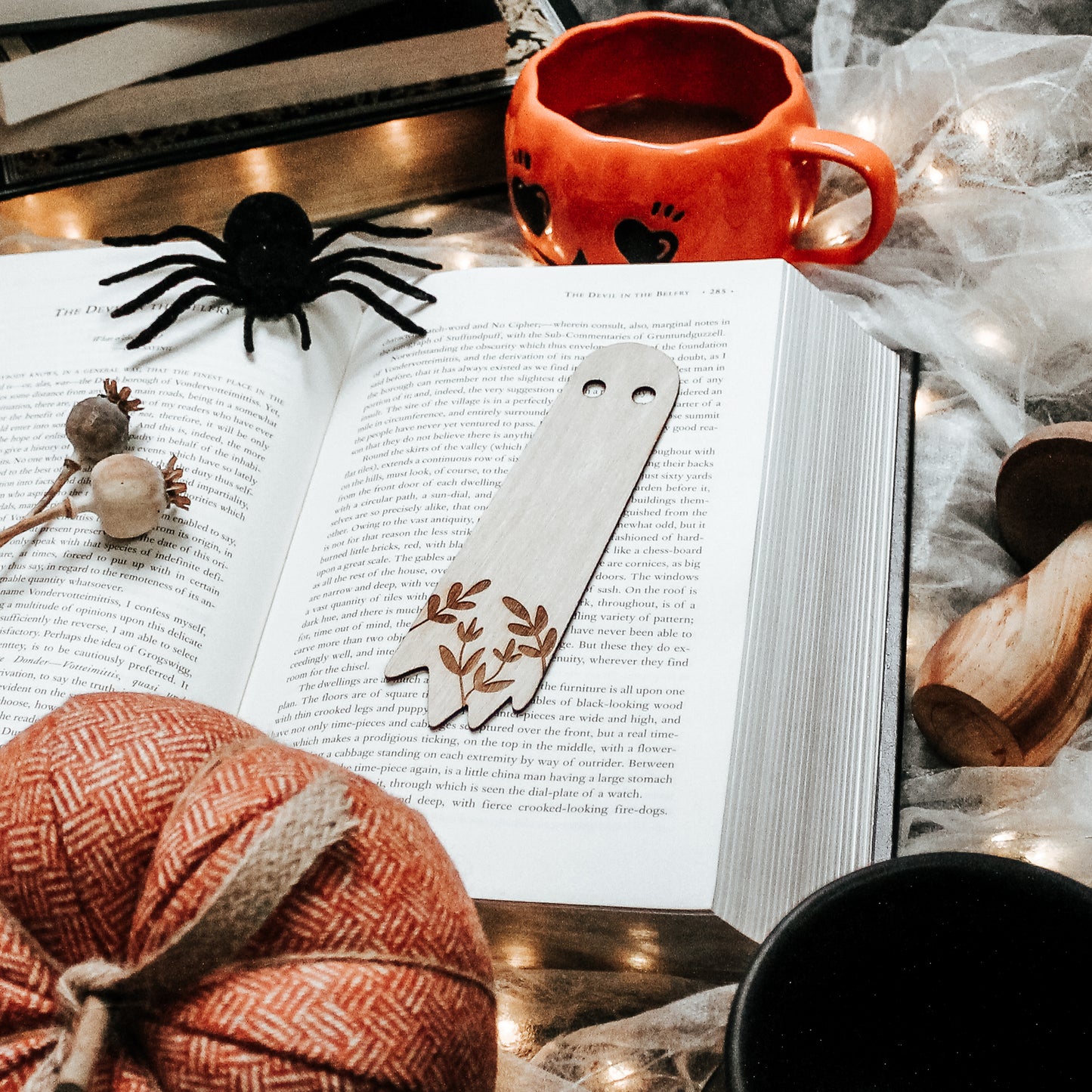 wooden engraved ghost bookmark laying on an open horror book surrounded by Halloween decor 
