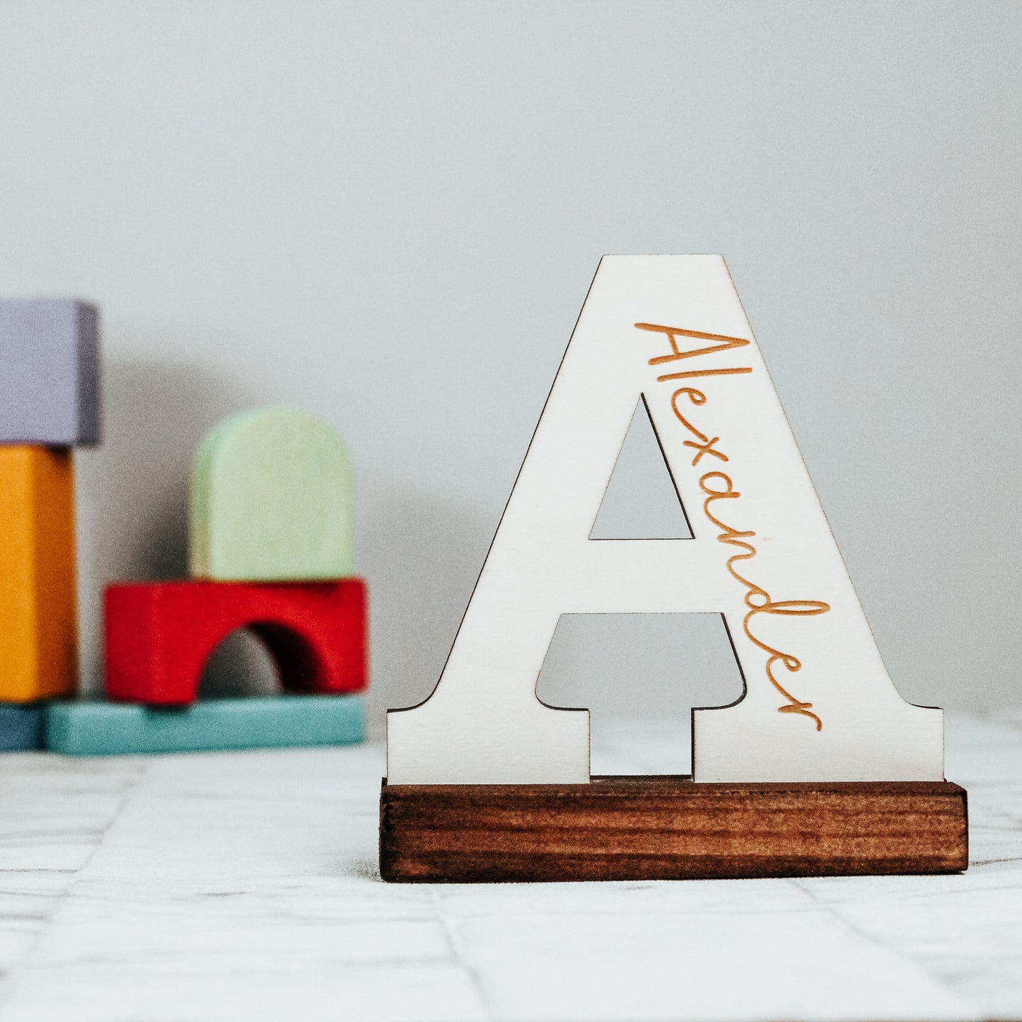 personalised wooden letter engraved with a name standing on a chunky wooden base, with natural colours and minimalistic aesthetic