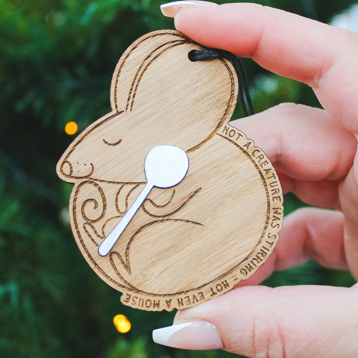 Wooden mouse ornament with a spoon, held by a hand against a blurred green background.
