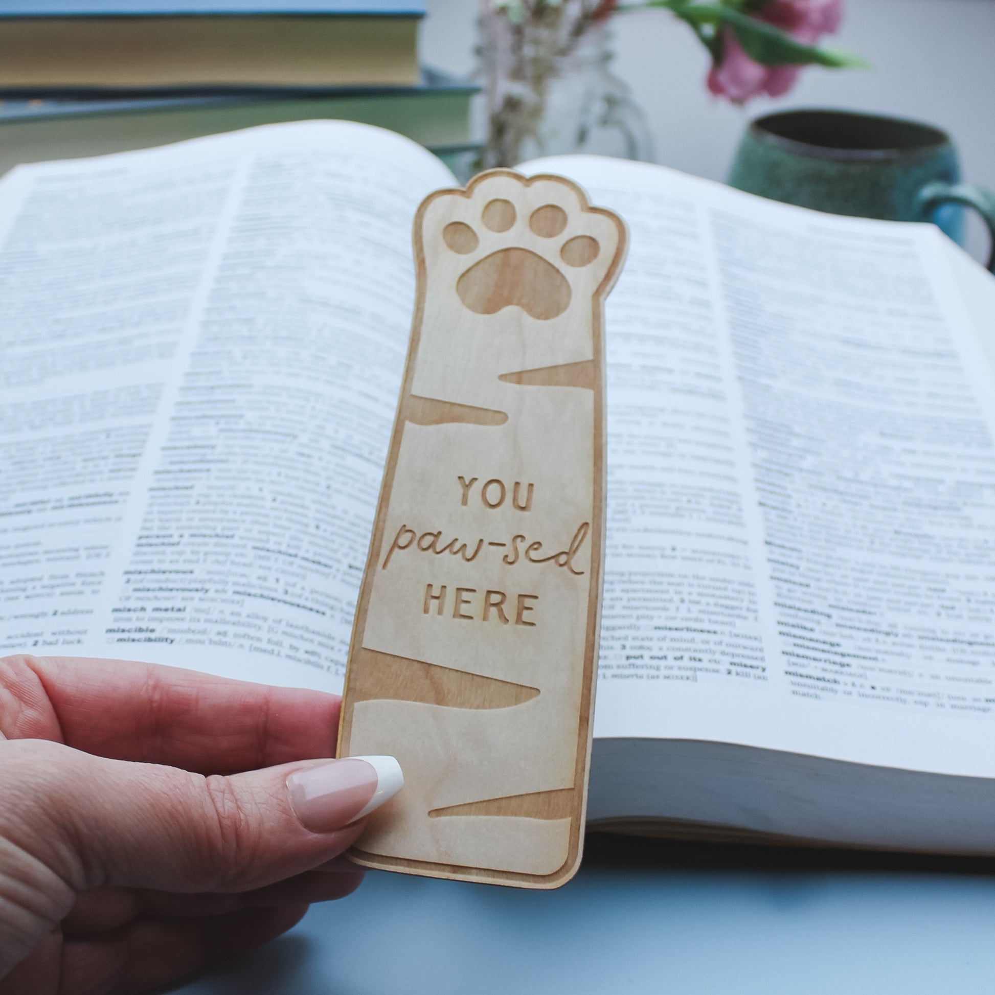 Wooden bookmark with paw print design held over an open book