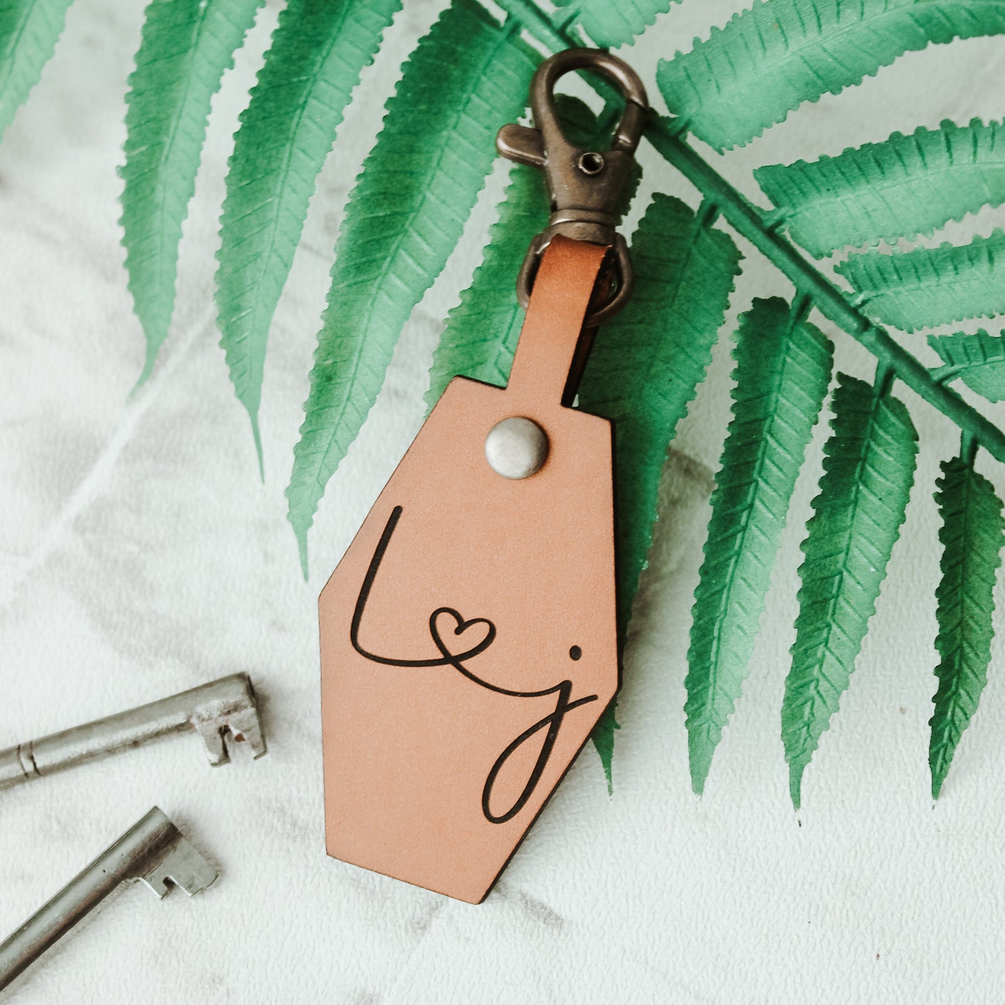whisky coloured brown leather keyring with initials engraved on it connected by a heart design. with a swivel clasp attached to clip onto keys or a bag 