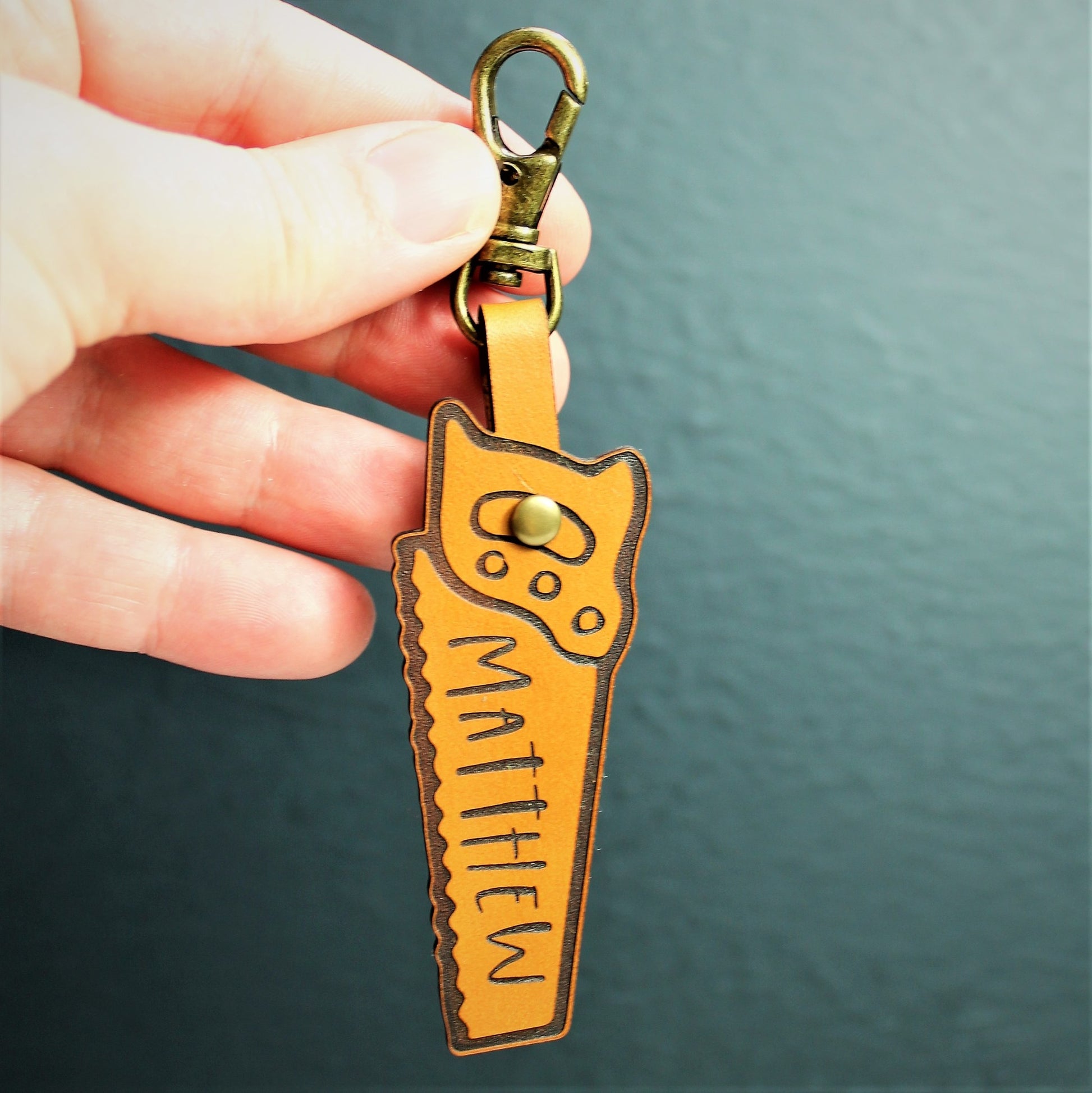 hand holding a leather saw shaped keyring with brass clasp with customised name 