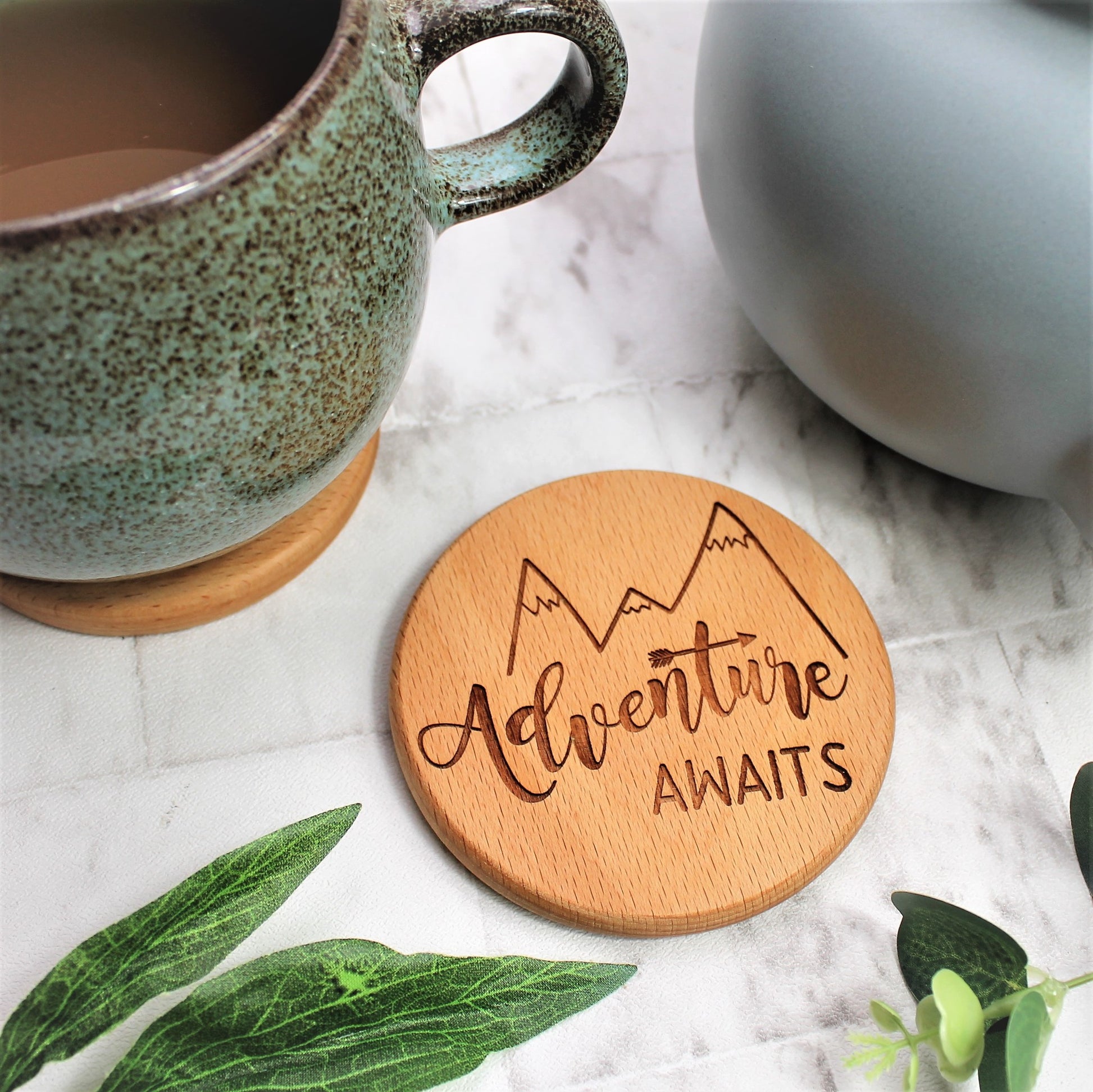 wooden engraved coaster with the quote adventure awaits on and a mountain design