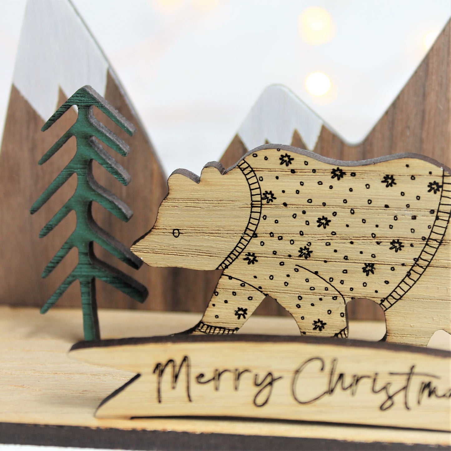 3d wooden ornament with mountain and forest scene, and a festive jumper bear