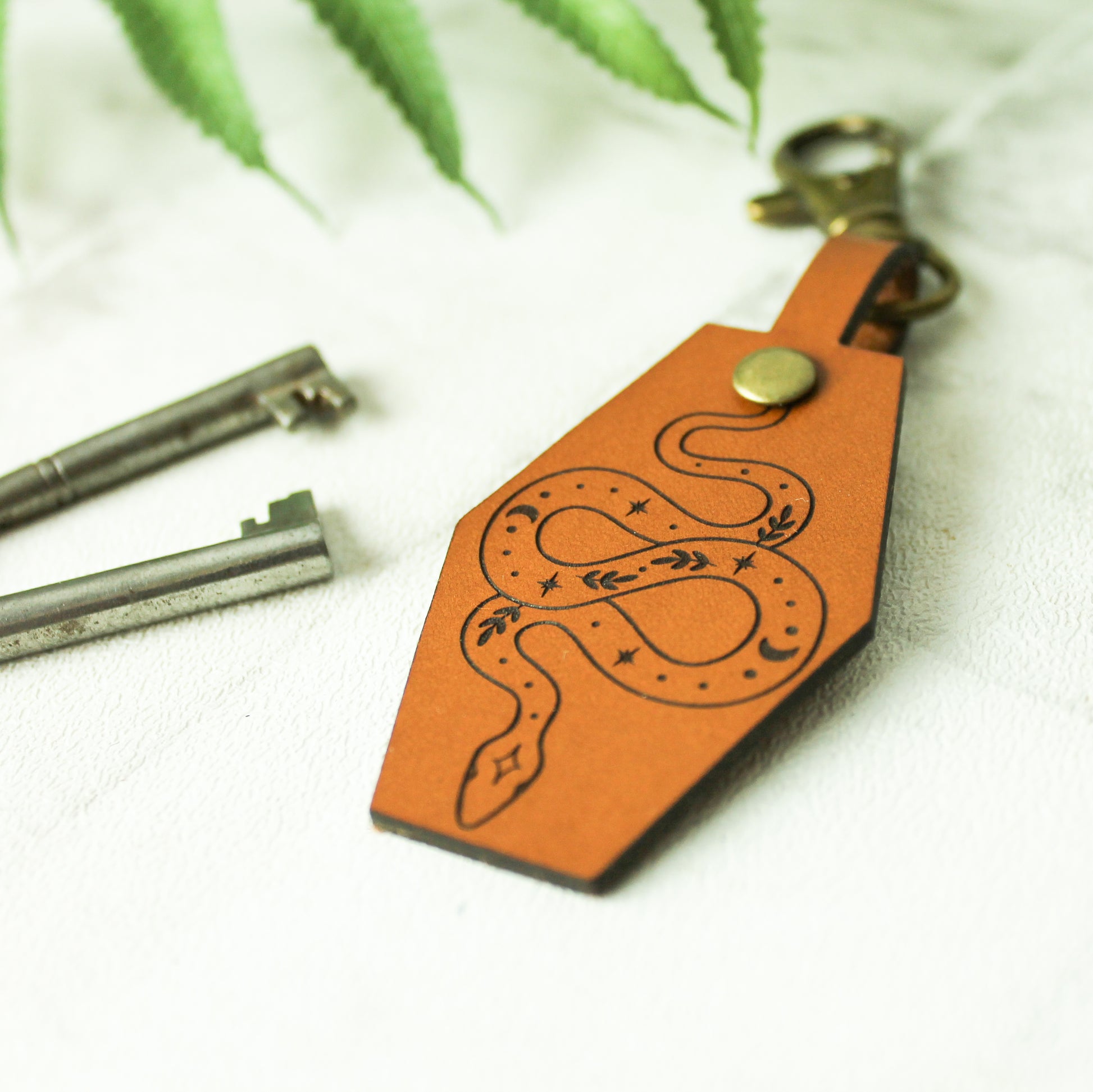 real leather keyring in a whisky colour engraved with a celestial snake design with botanical elements 